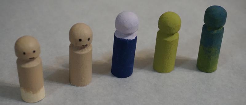 A line of clothespin dolls in various states of painted base completion. Some are purple or mottled green.